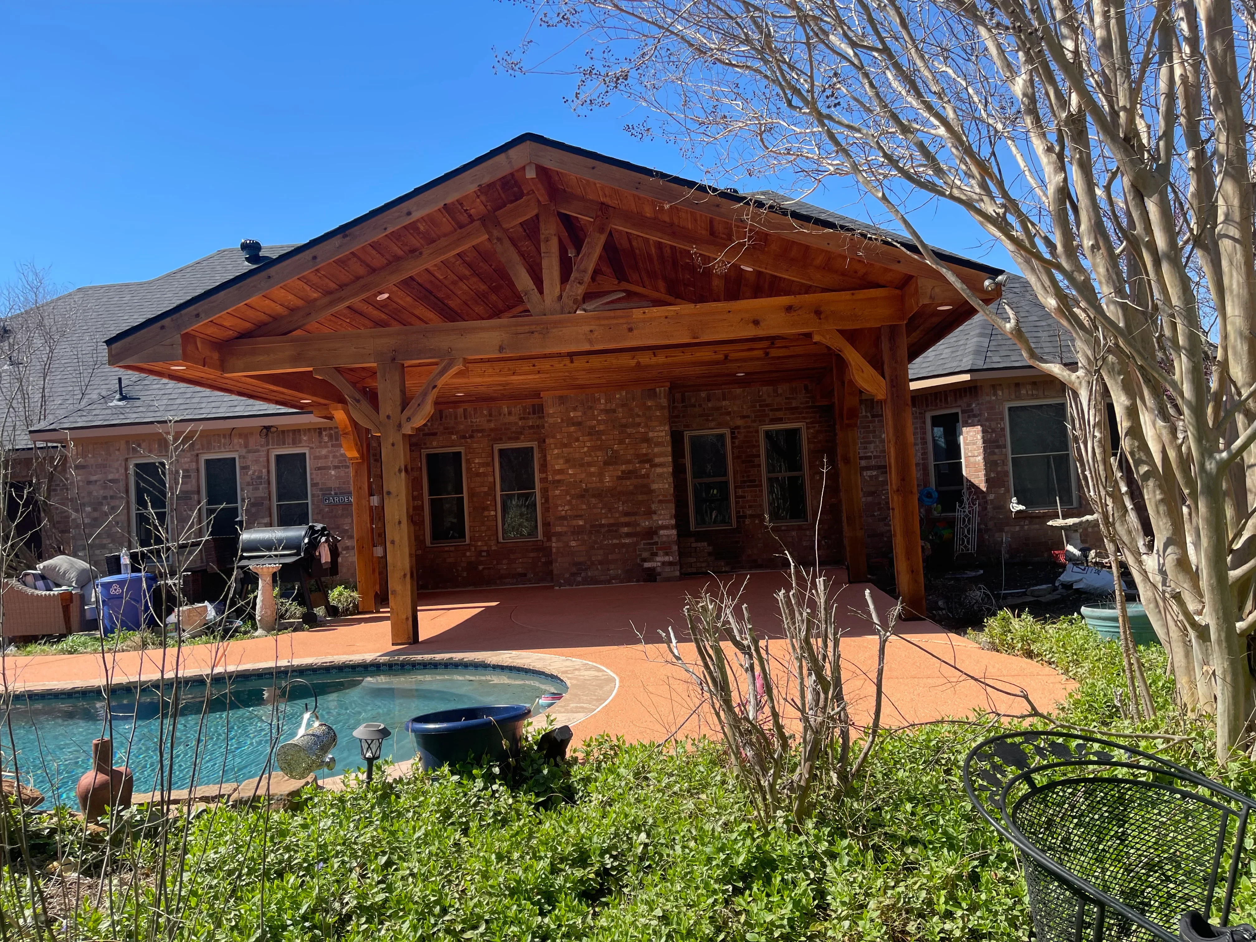 Timber frame patio cover with exposed beams over brick home and pool deck