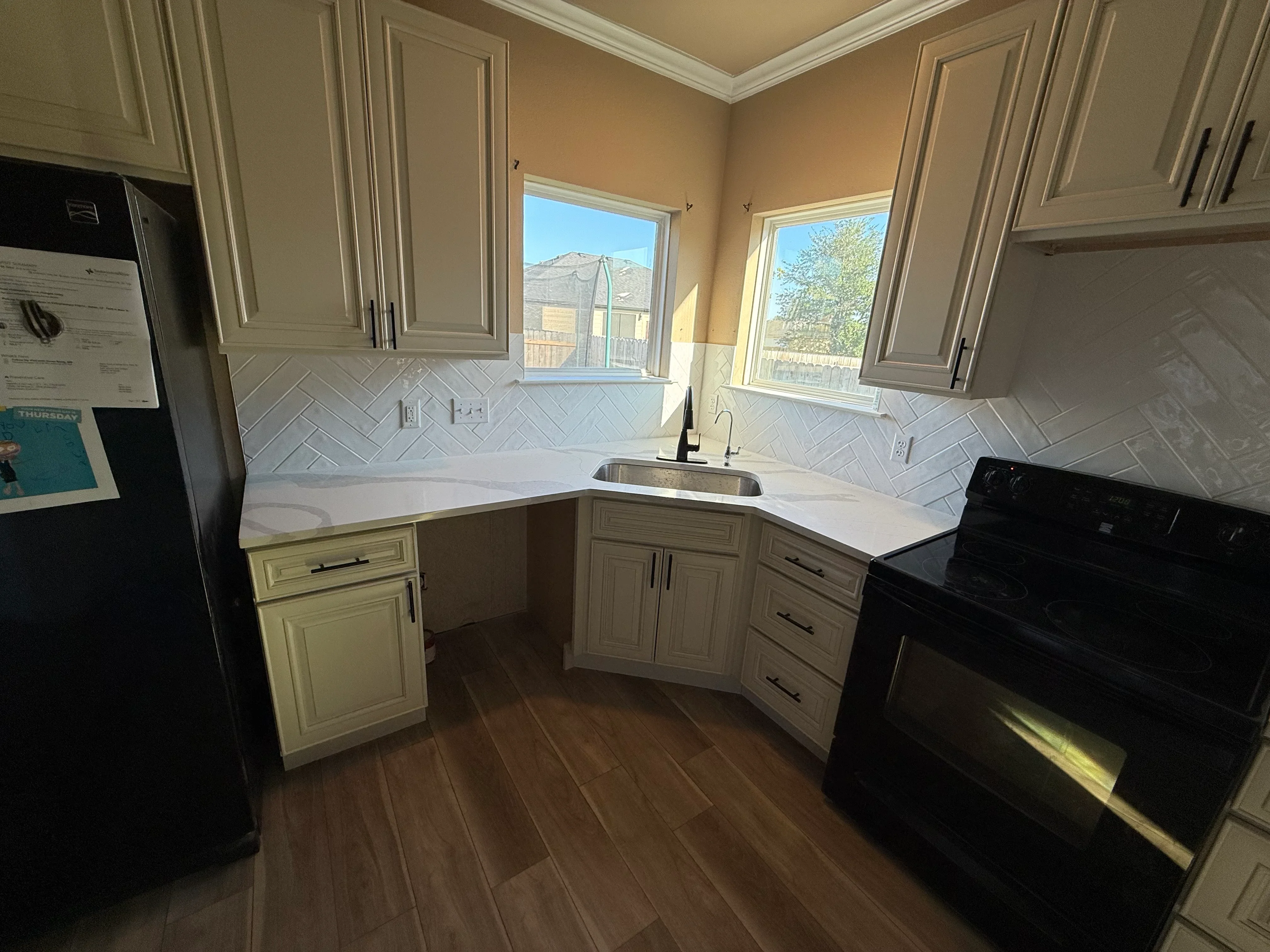 Kitchen with cream cabinetry, white quartz counters, herringbone tile backsplash, and hardwood floors