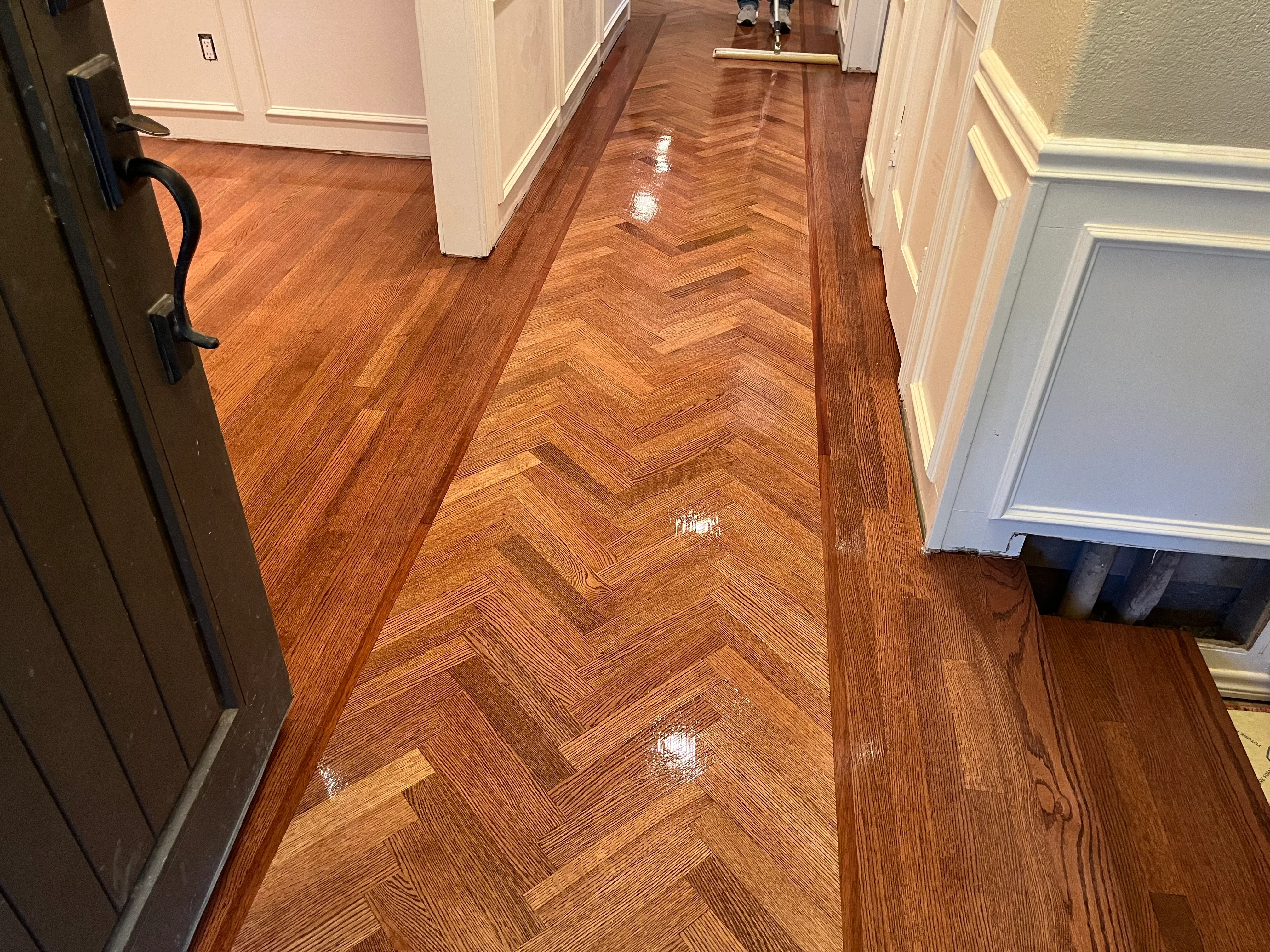 Herringbone hardwood floor with restored finish and water damage repair in hallway