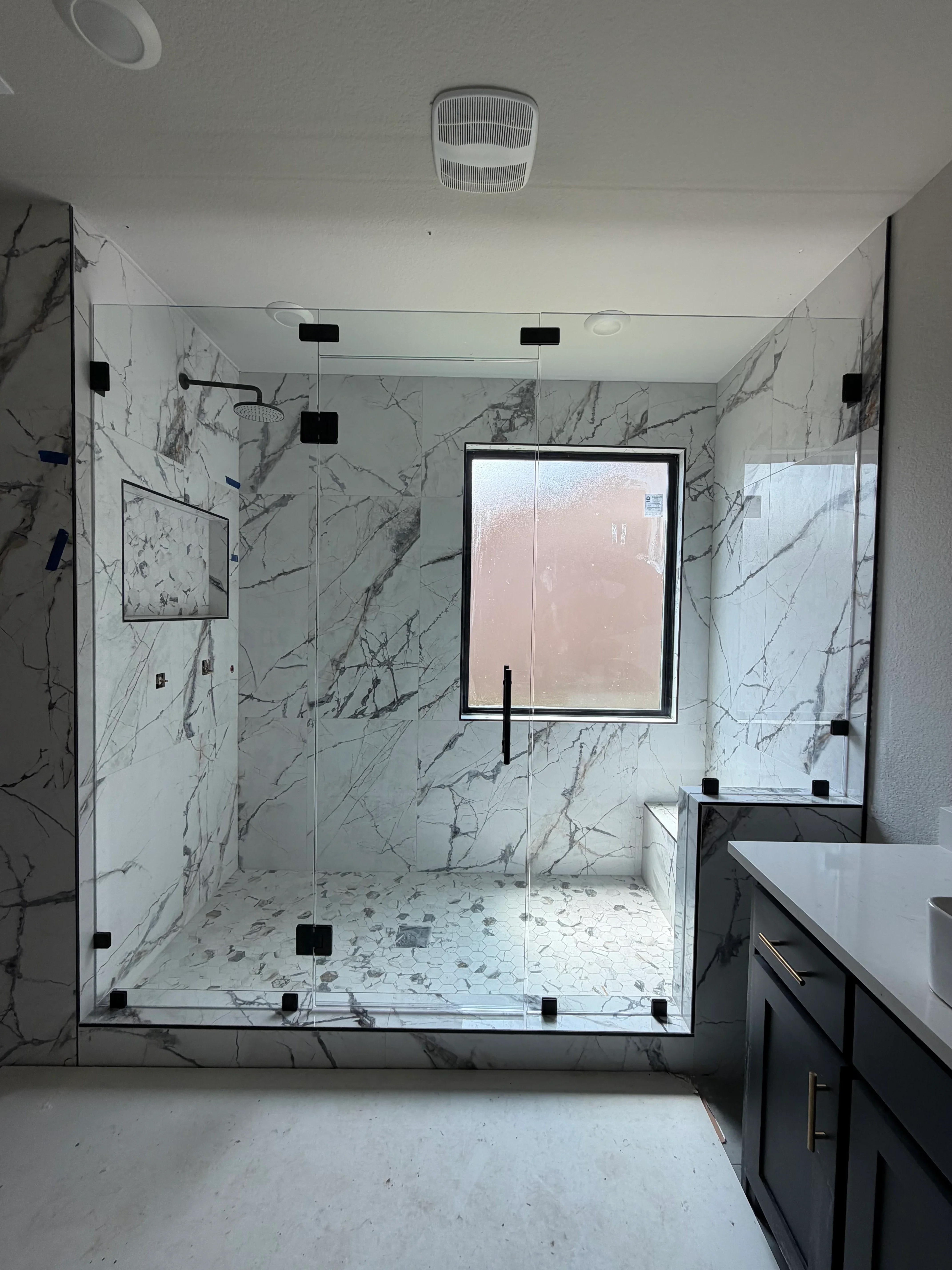 White marble shower with gray veining, frameless glass doors, black hardware, and linear drain