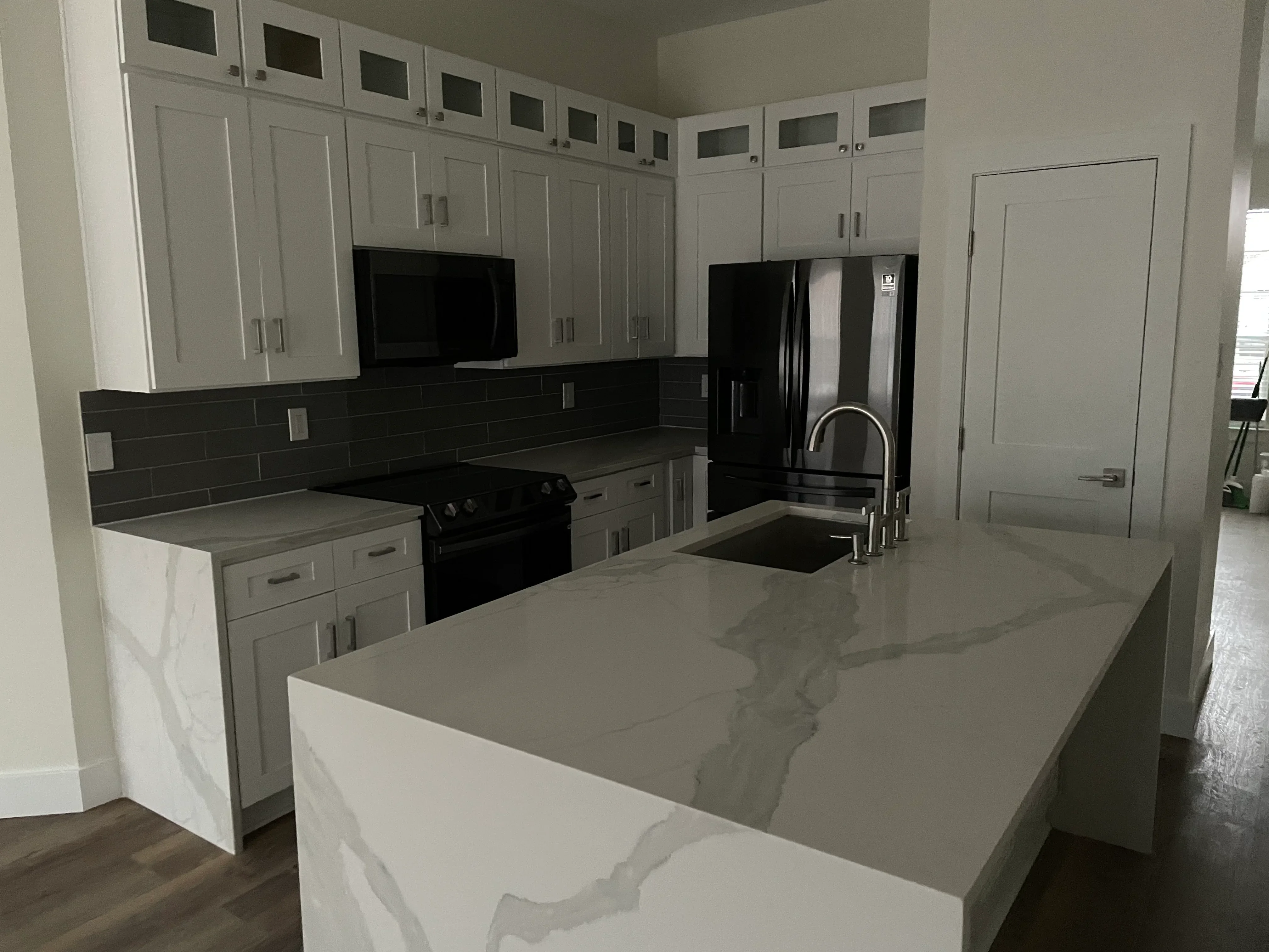 Modern kitchen with white cabinets, gray quartz counters, black subway tile backsplash, and black stainless appliances