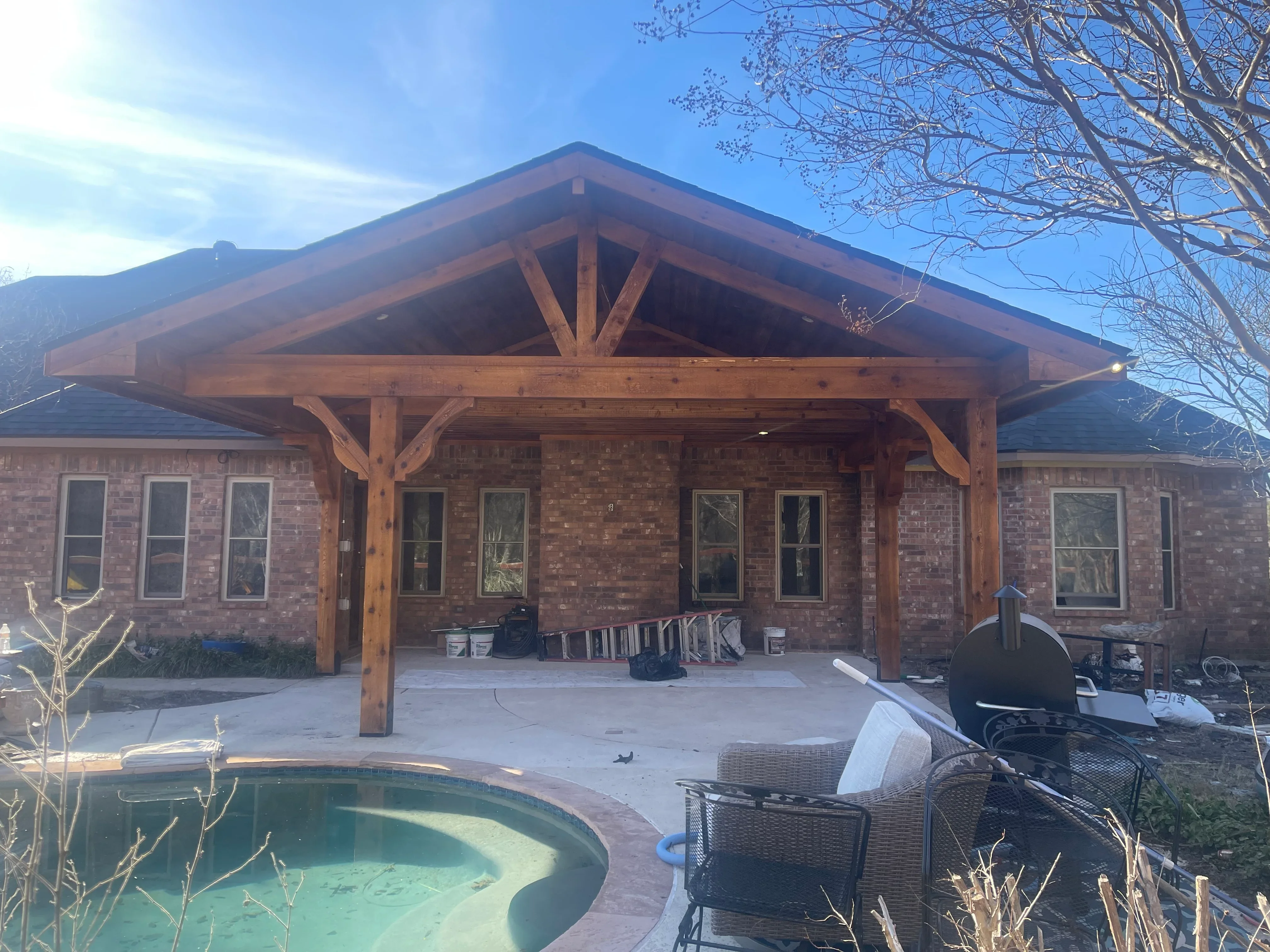 Timber frame patio cover with exposed beams and gabled roof over brick home