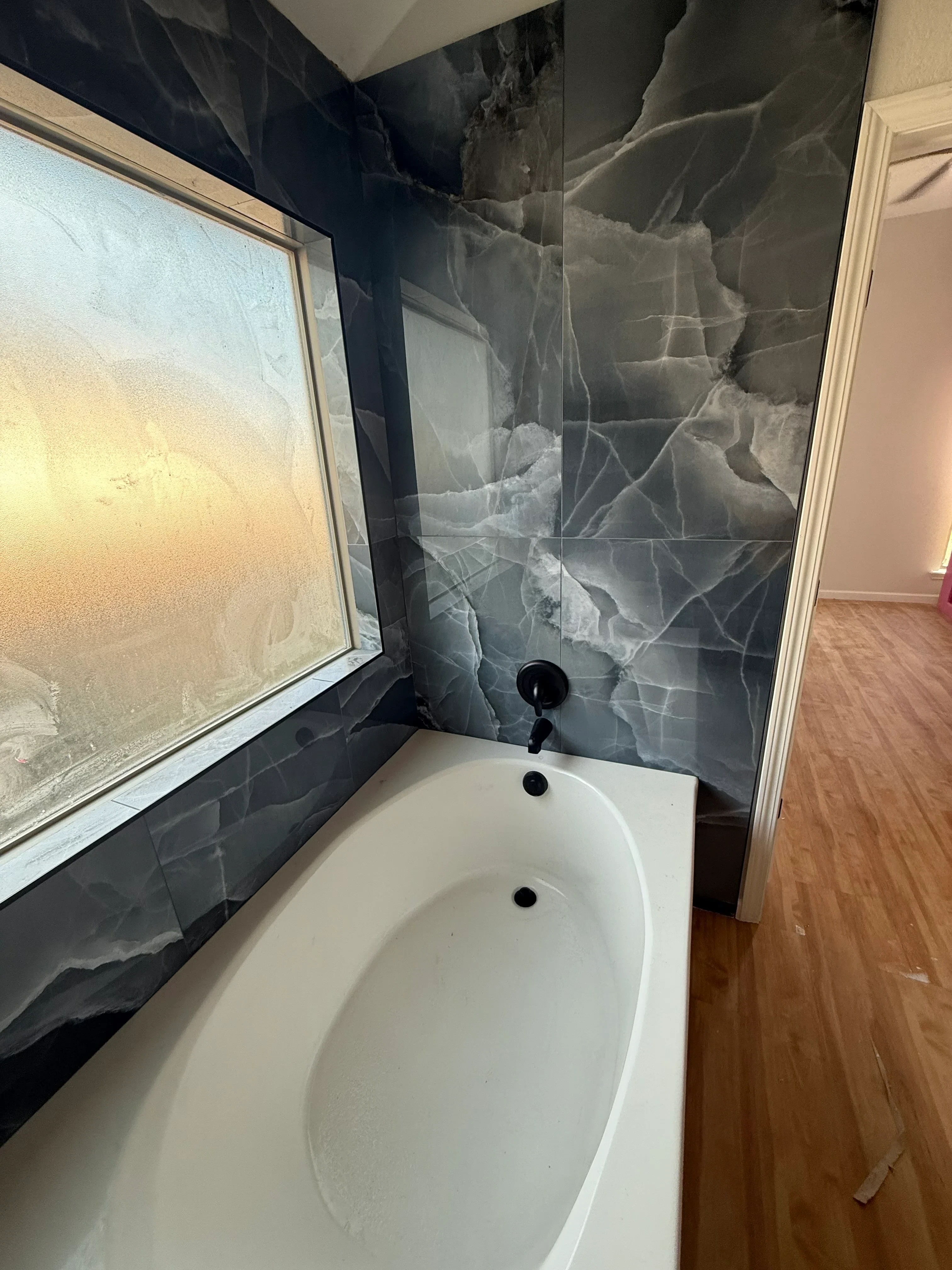 Restored bathroom with dark marble tile walls, light stone floor tile, white vessel sink, and wood ceiling
