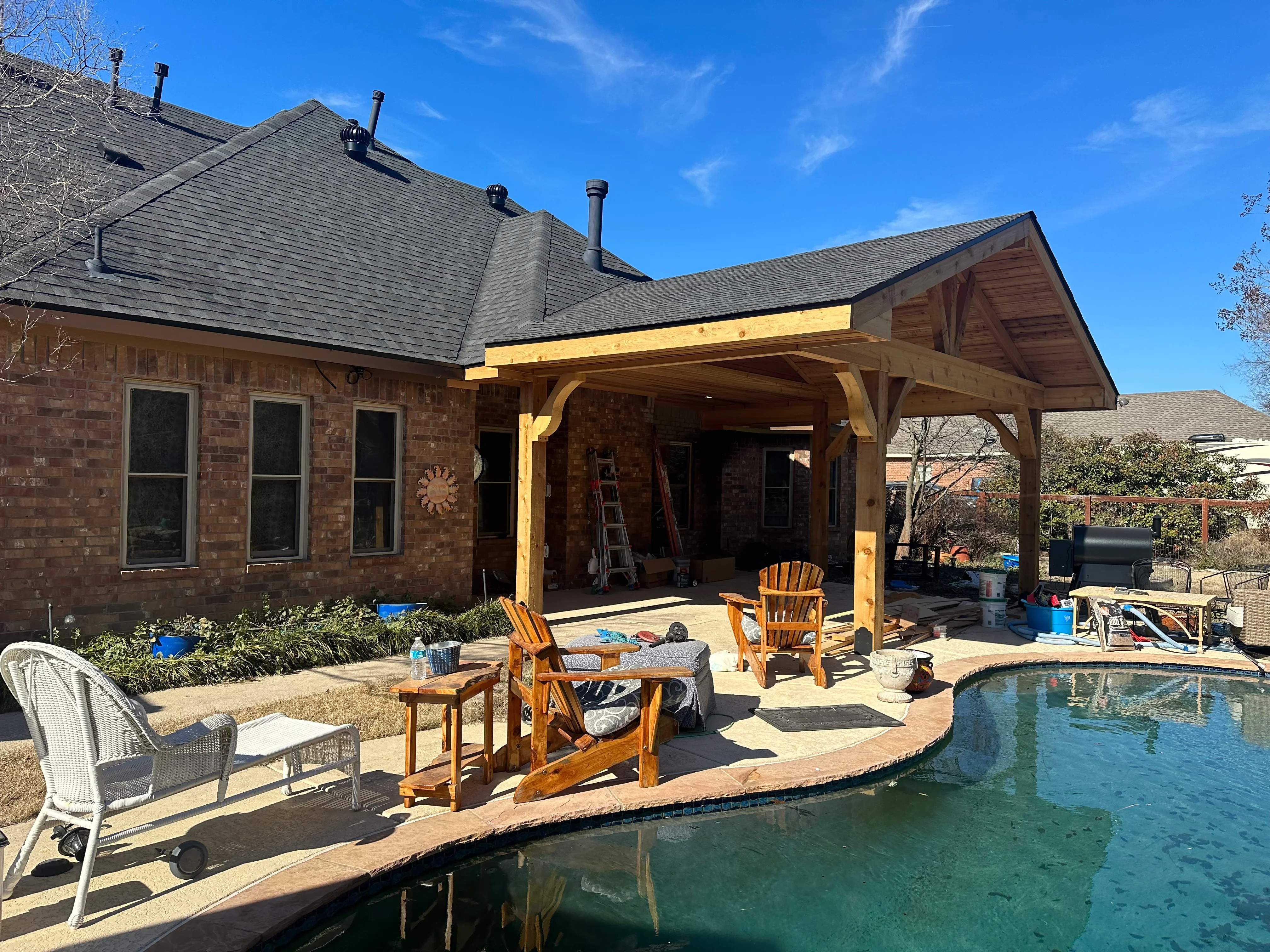 Timber-frame covered patio with exposed beams attached to brick home overlooking pool