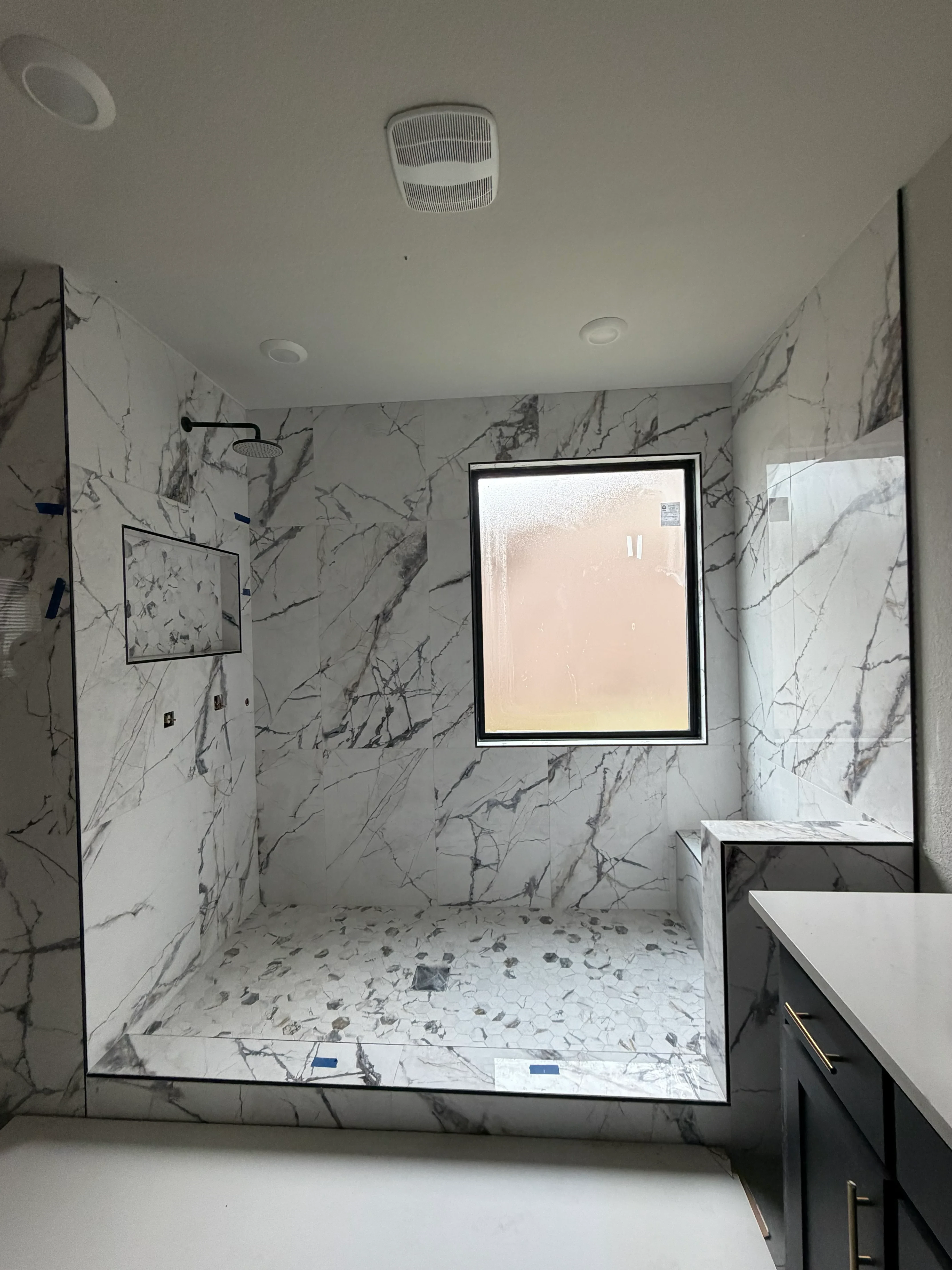 Marble-look porcelain tile shower enclosure with frameless glass door and recessed lighting