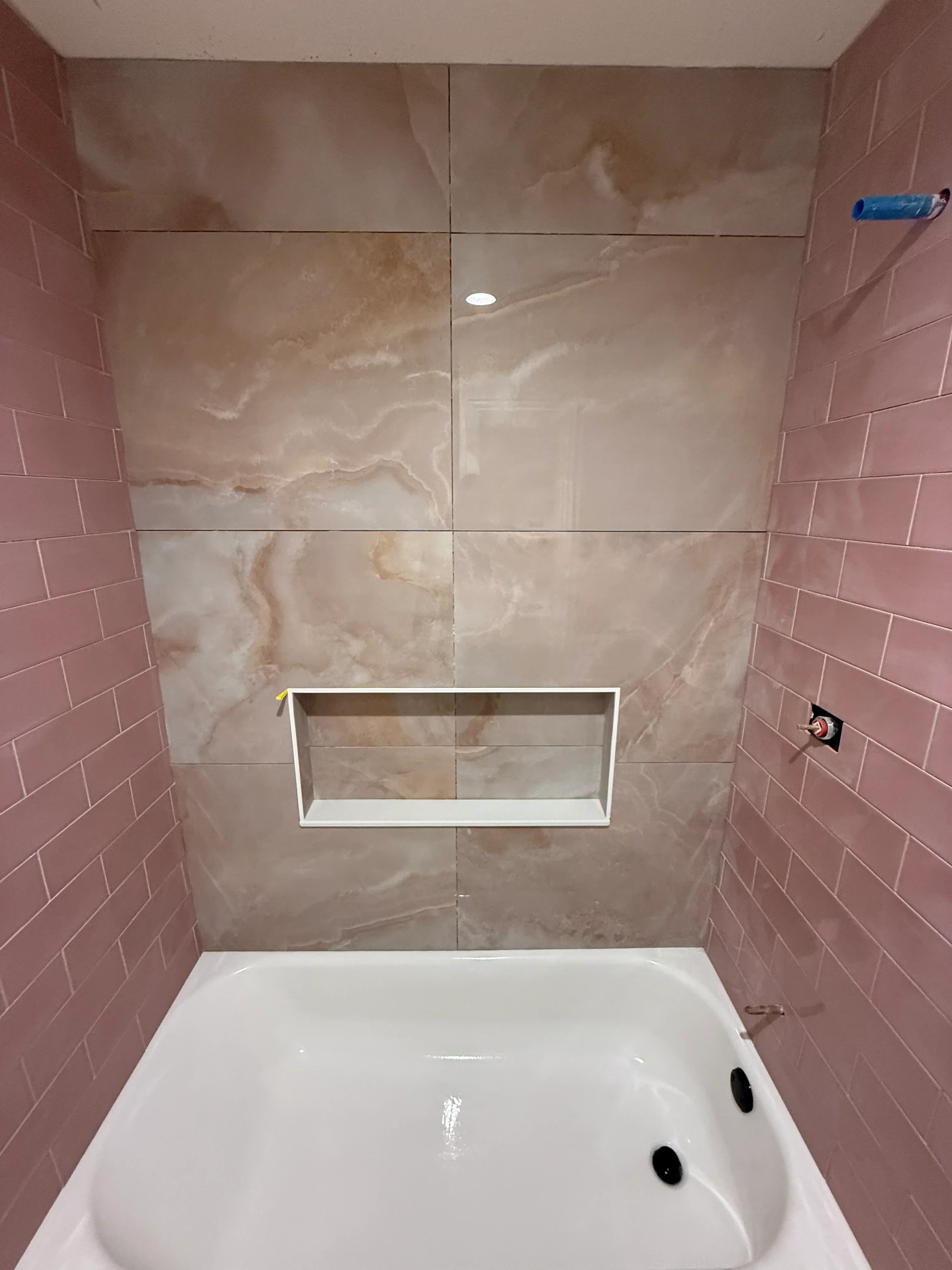 Restored bathroom with marble ceramic tile walls, herringbone floor pattern, white soaking tub, and recessed fixtures