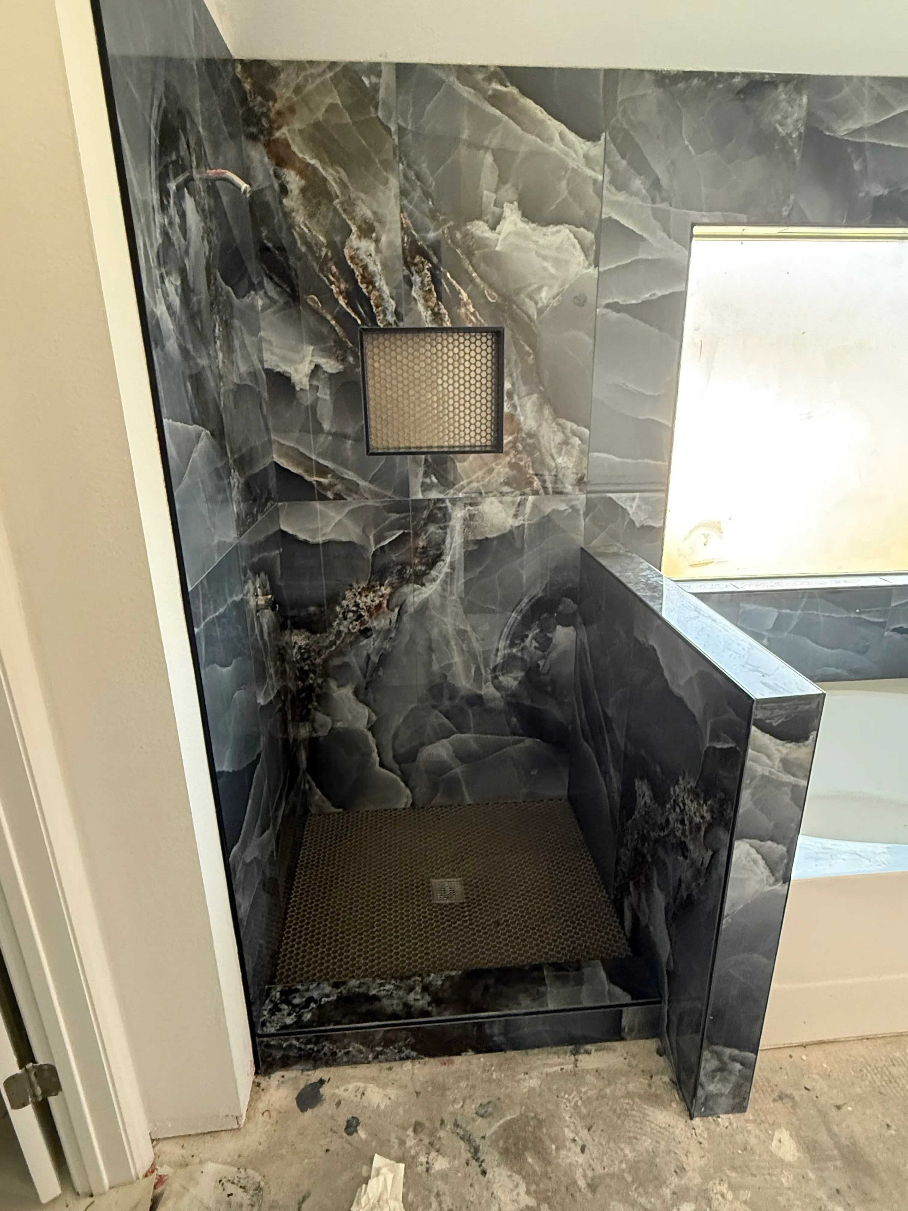 Black and gray marble backsplash with polished granite countertop and stainless steel range hood