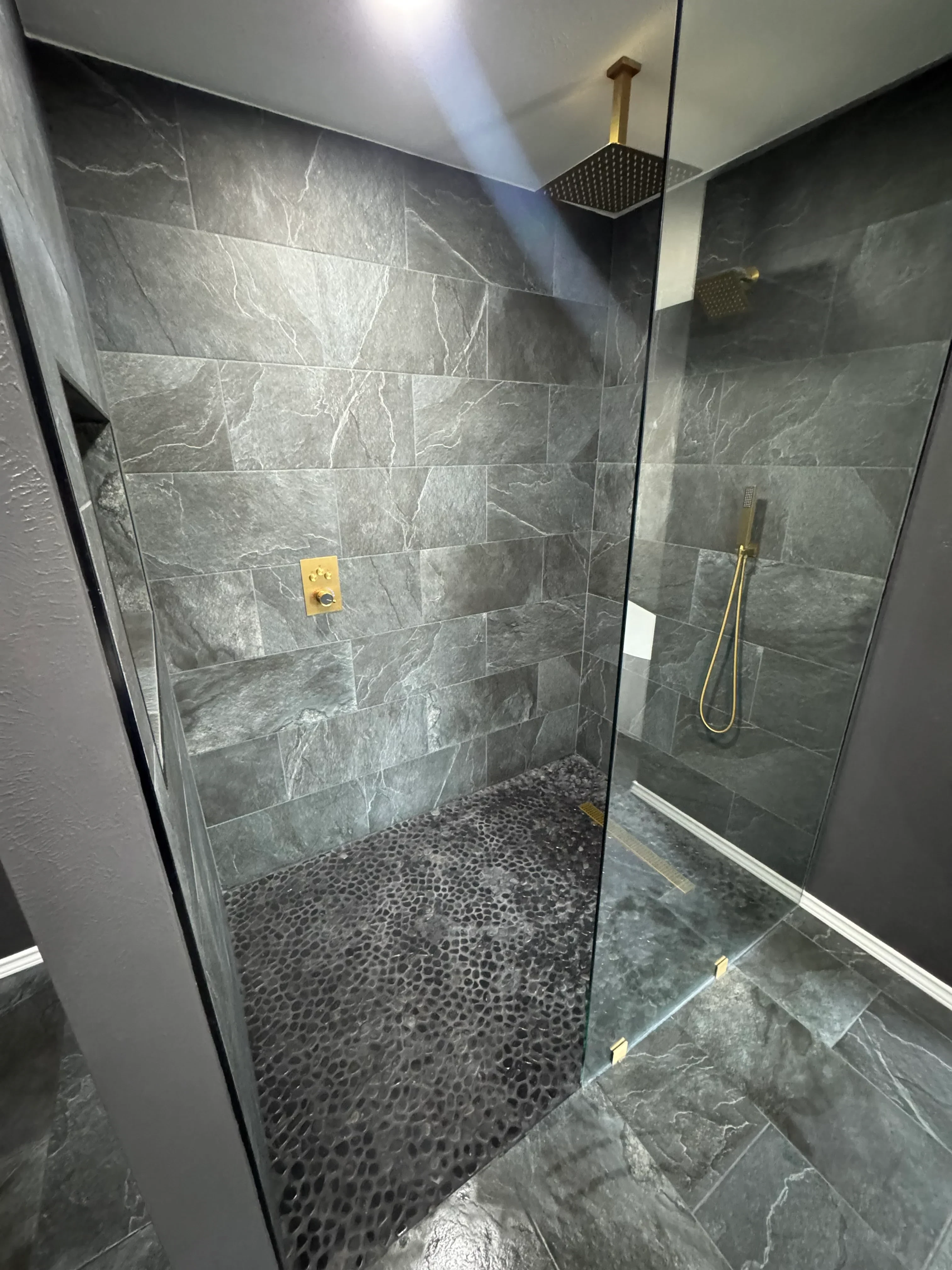 Gray slate tile shower with pebble stone accent wall and brass fixtures