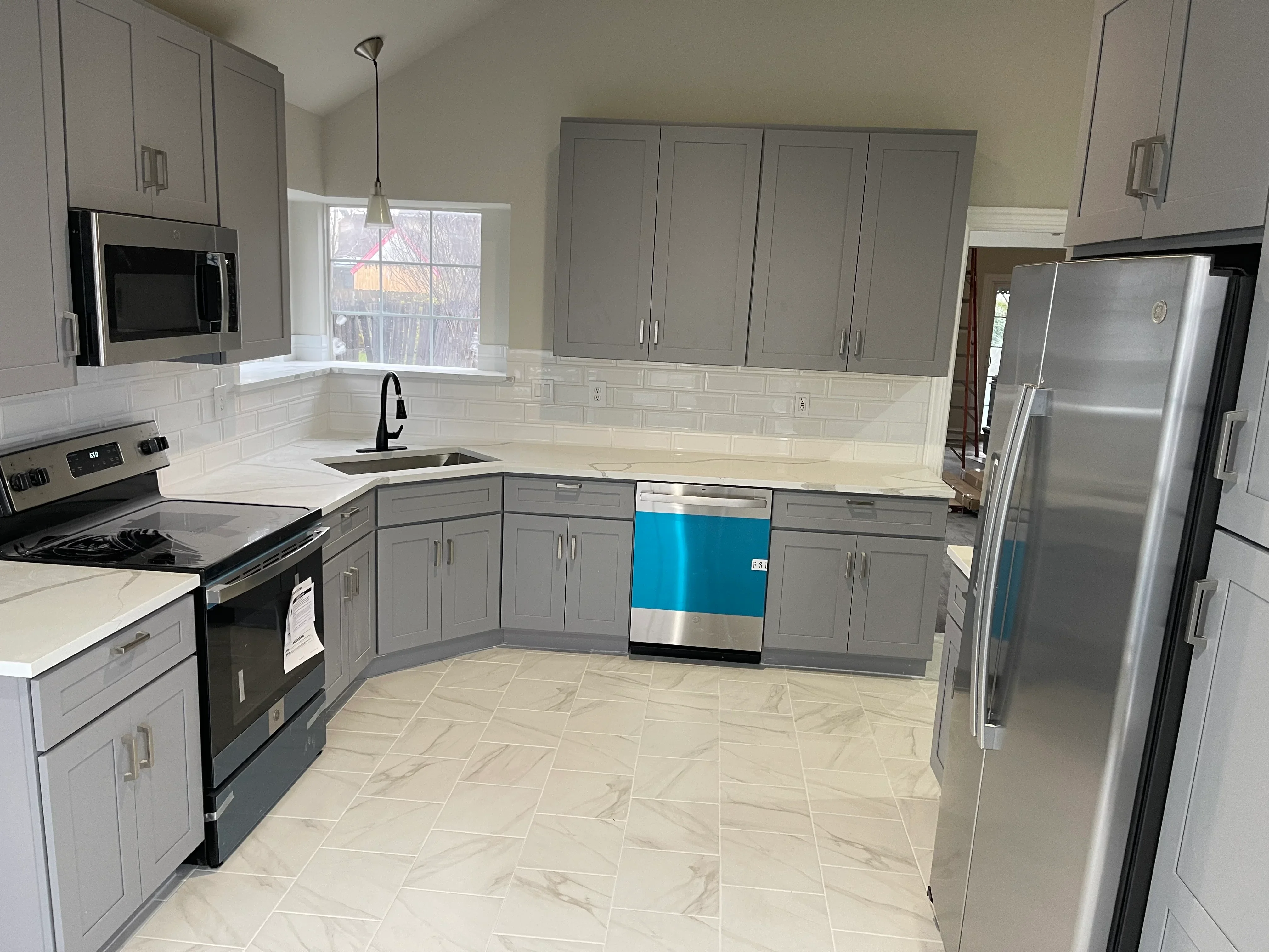 Restored kitchen with gray cabinets, white subway tile backsplash, herringbone tile floor, and stainless steel appliances