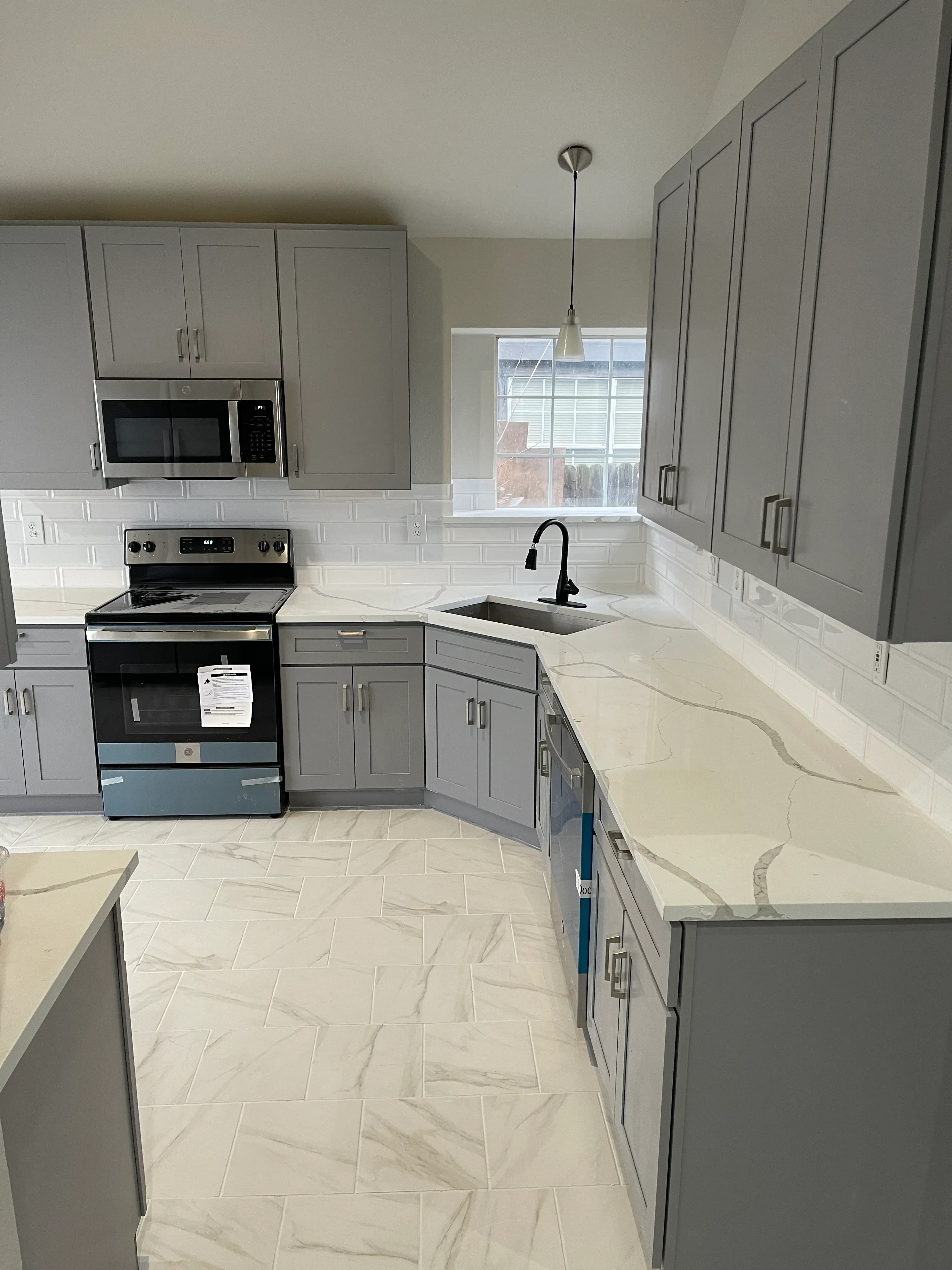 Restored kitchen with gray cabinetry, cream subway tile backsplash, stainless steel appliances and range hood