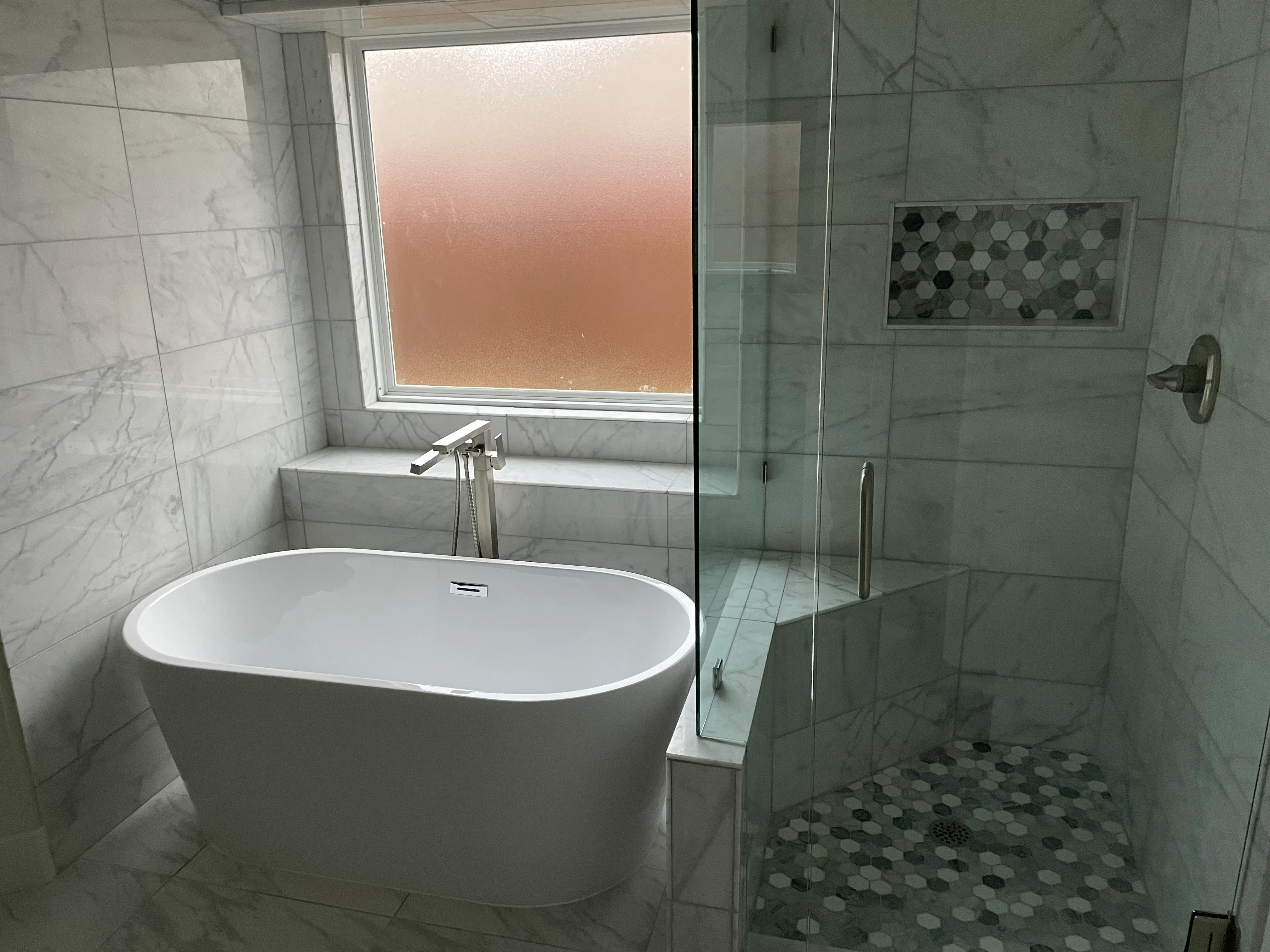 Marble tile bathroom with freestanding tub, frameless glass shower, and hexagonal mosaic floor