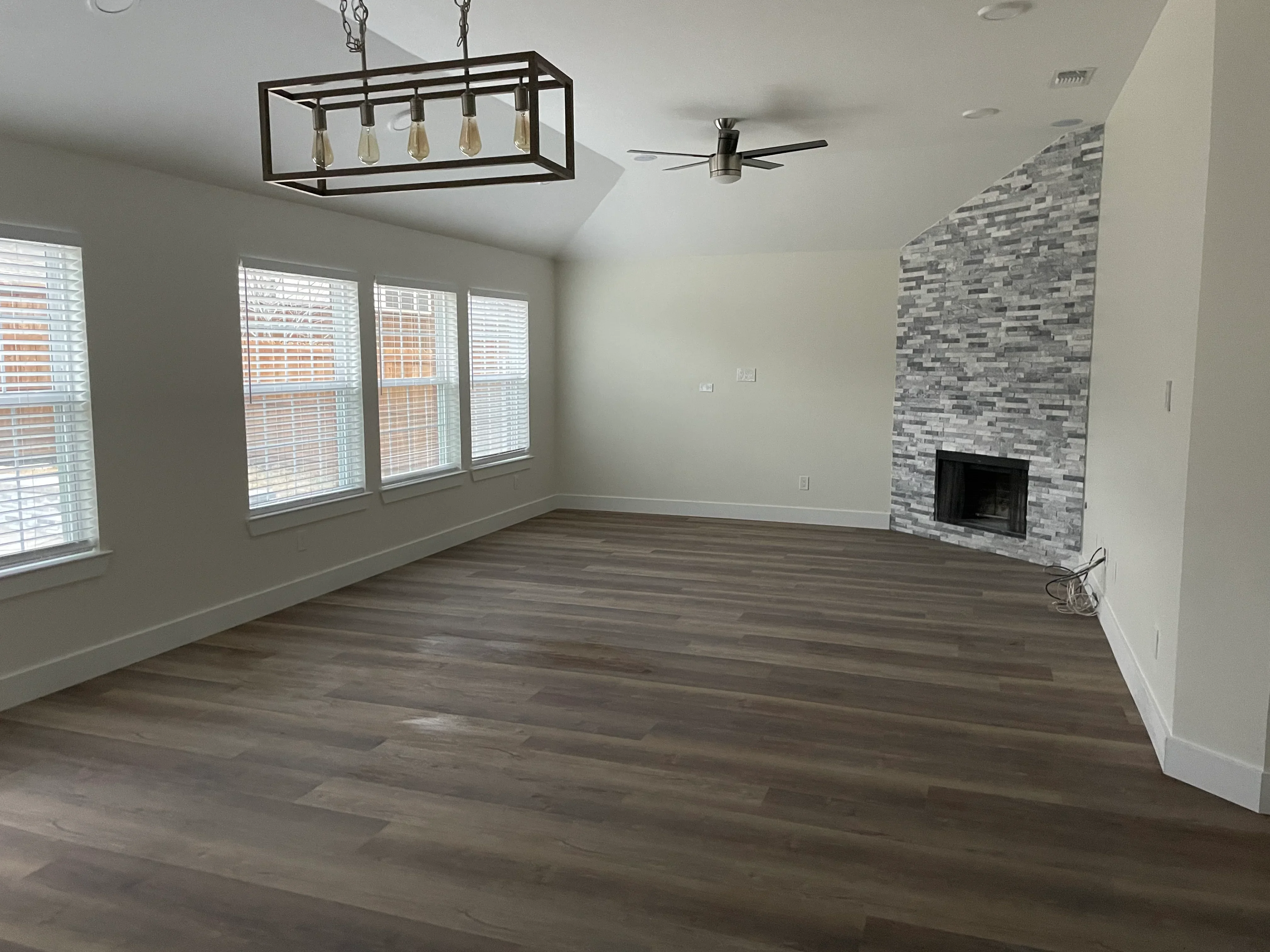 Restored living room with dark wood flooring, stone fireplace wall, and modern lighting fixtures