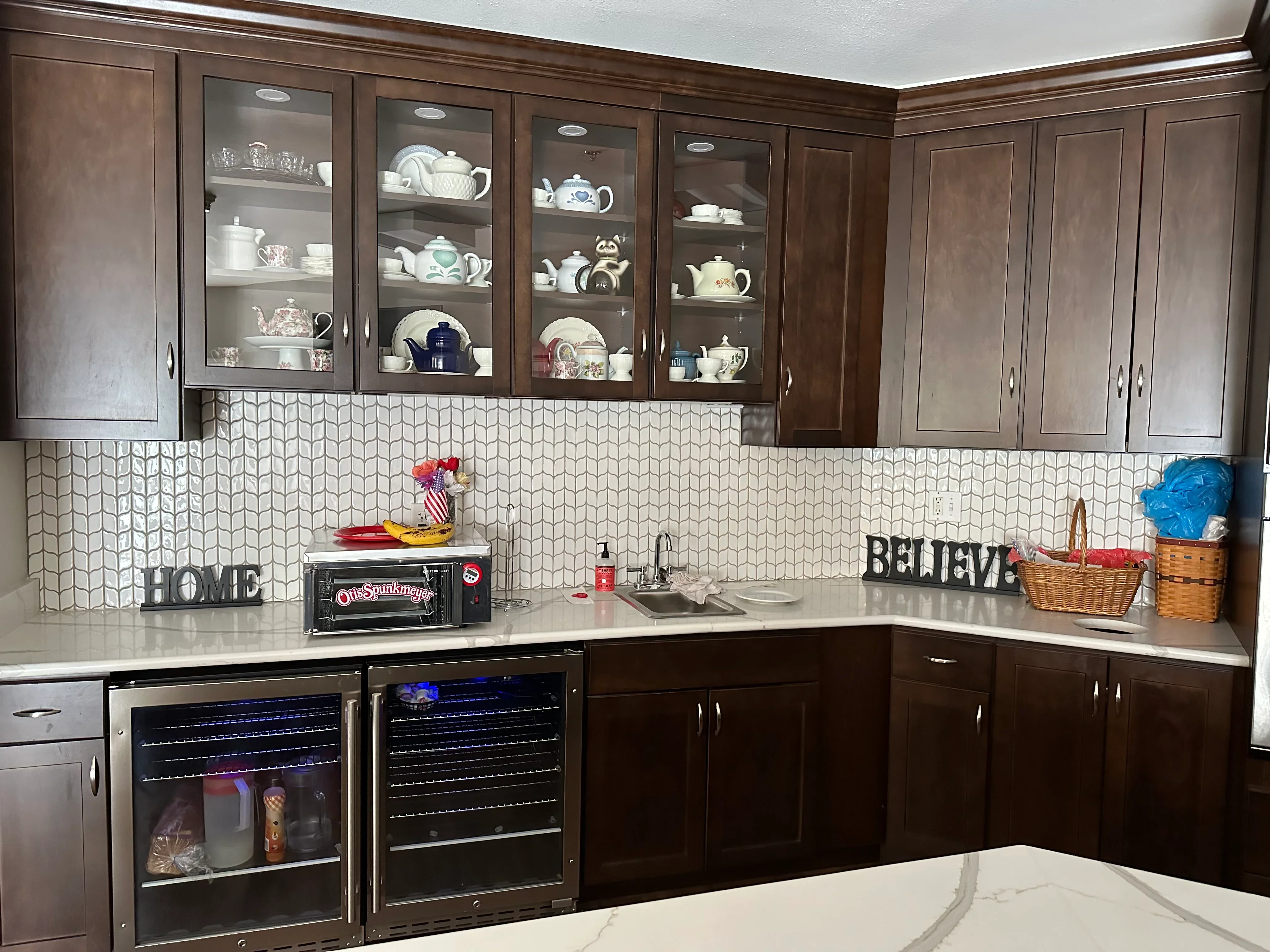 Two-tone kitchen with dark wood cabinets, glass-front upper cabinets, geometric white backsplash tile, and white quartz countertops