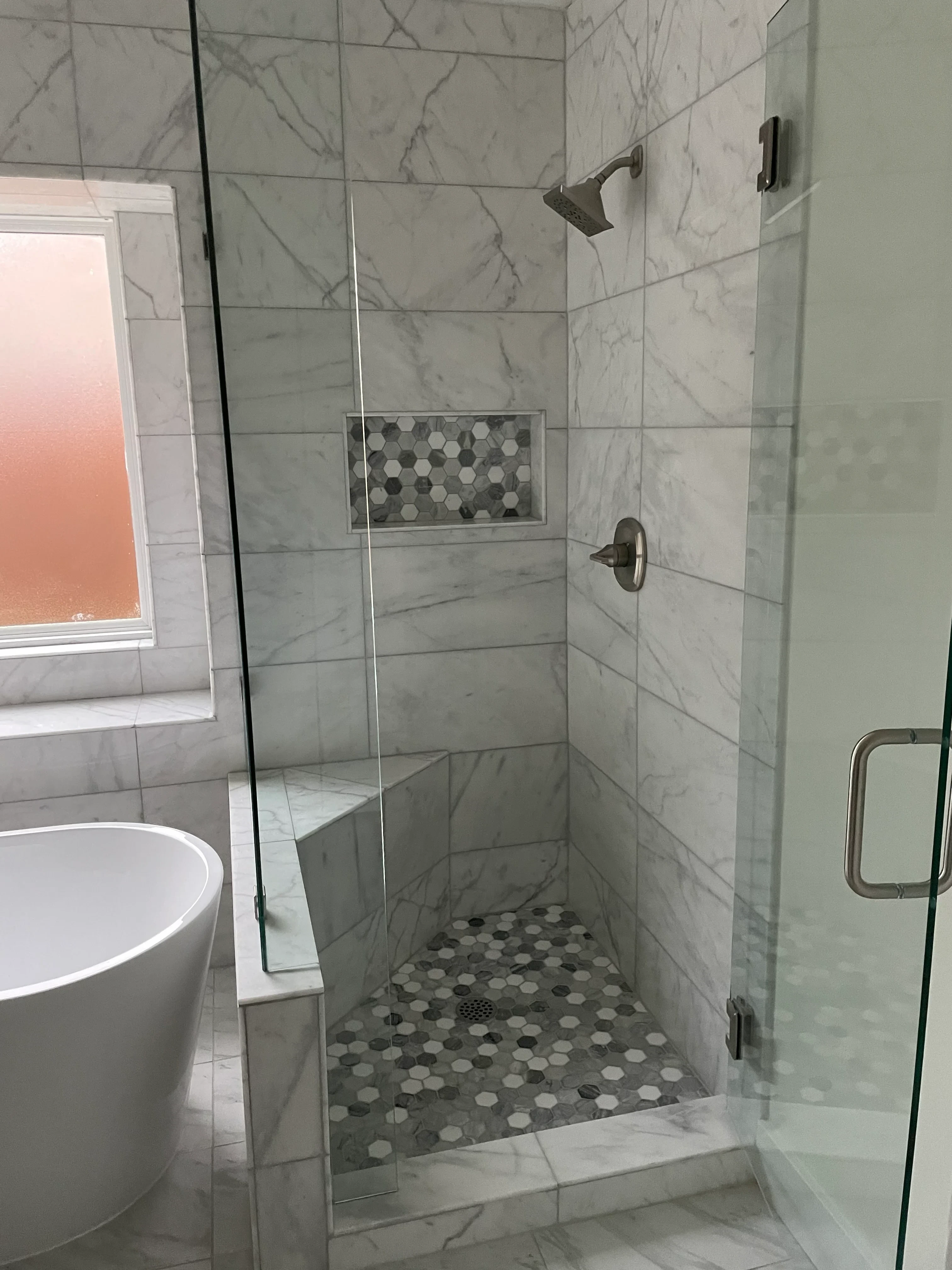 Marble tile bathroom with hexagonal mosaic accent wall and frameless glass shower enclosure