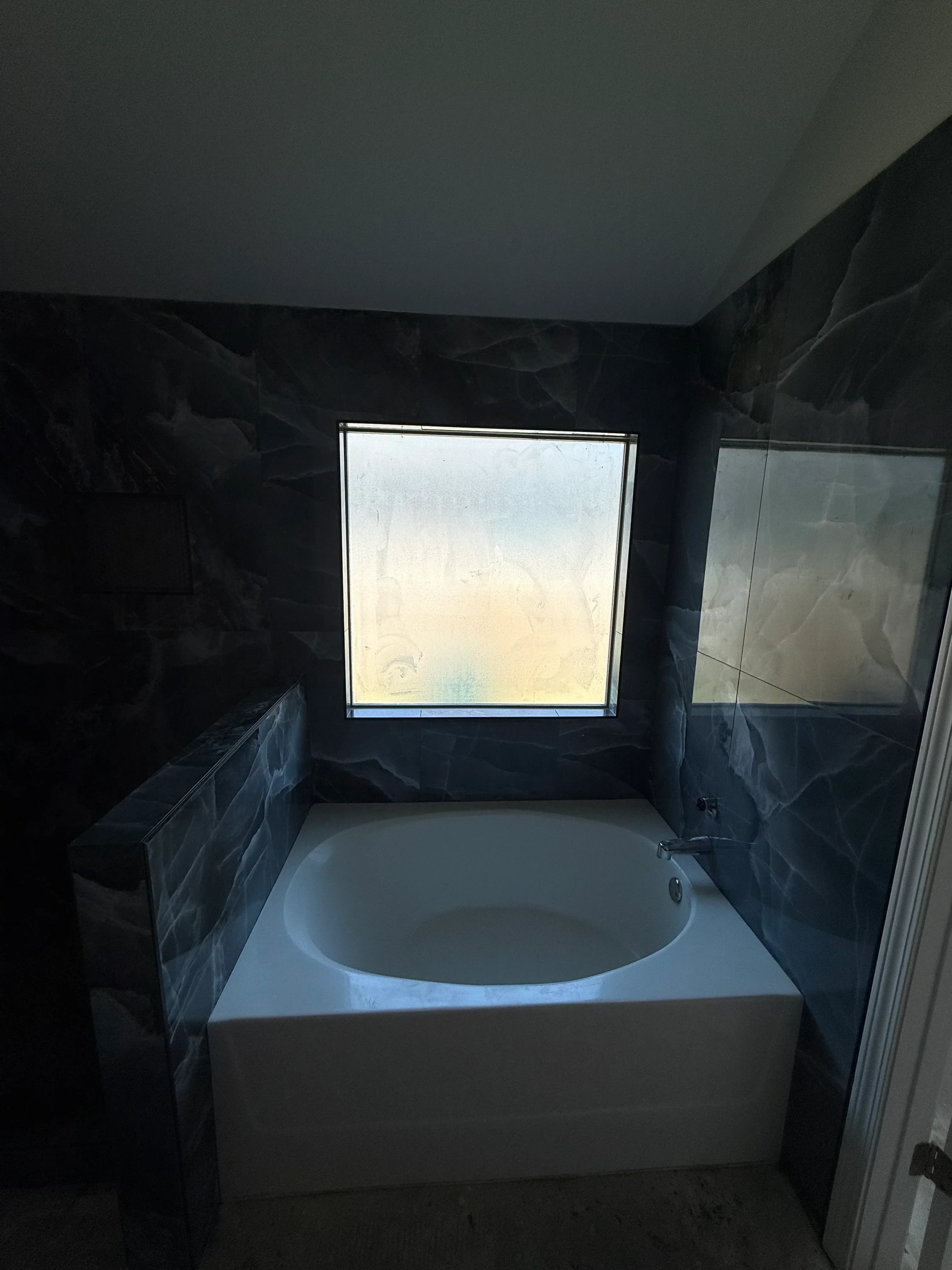 Restored bathroom with dark tile walls and floor, white oval sink, and framed mirror