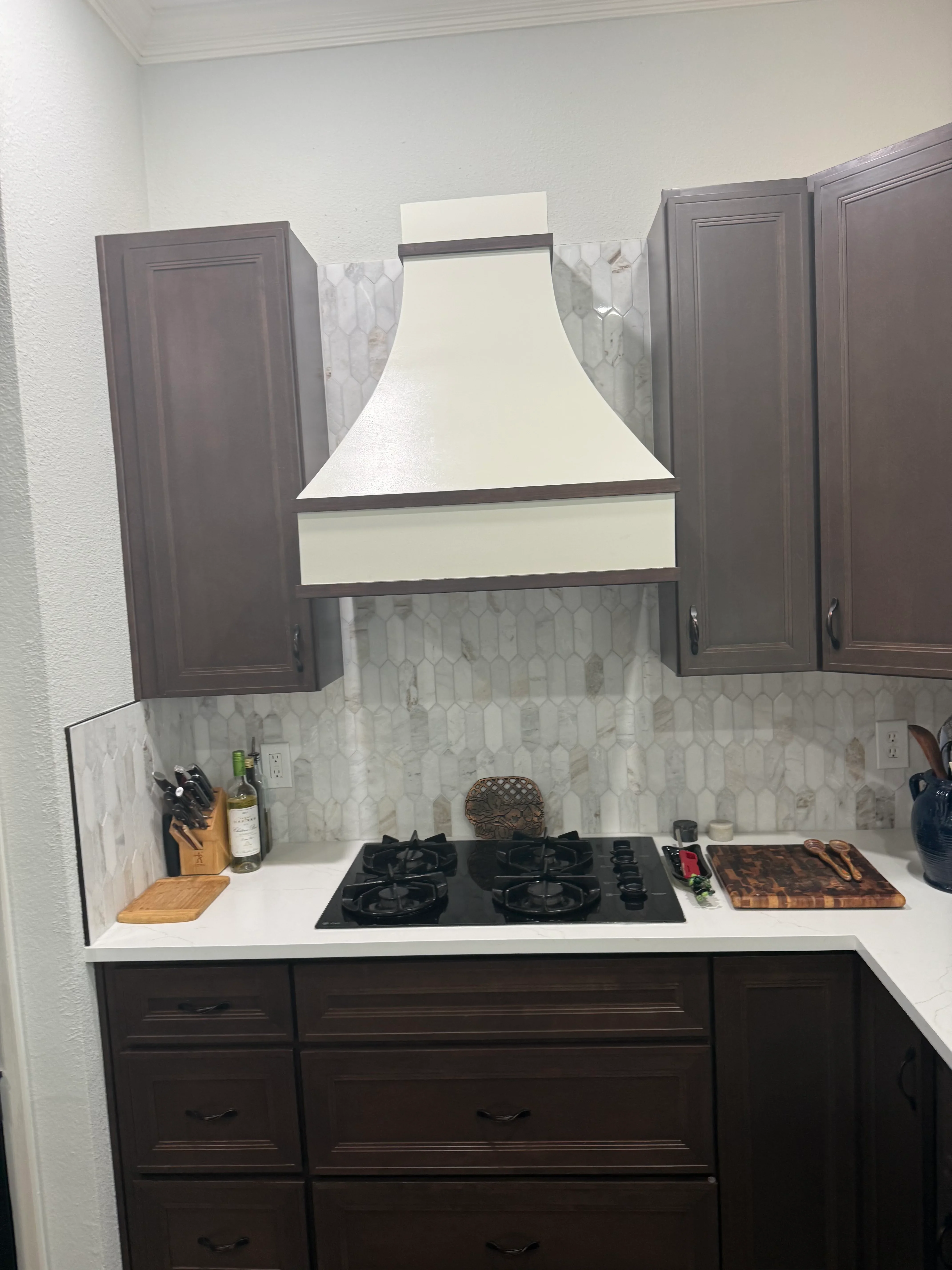 Kitchen with marble hexagon backsplash, white quartz counters, dark wood cabinets, and cream range hood