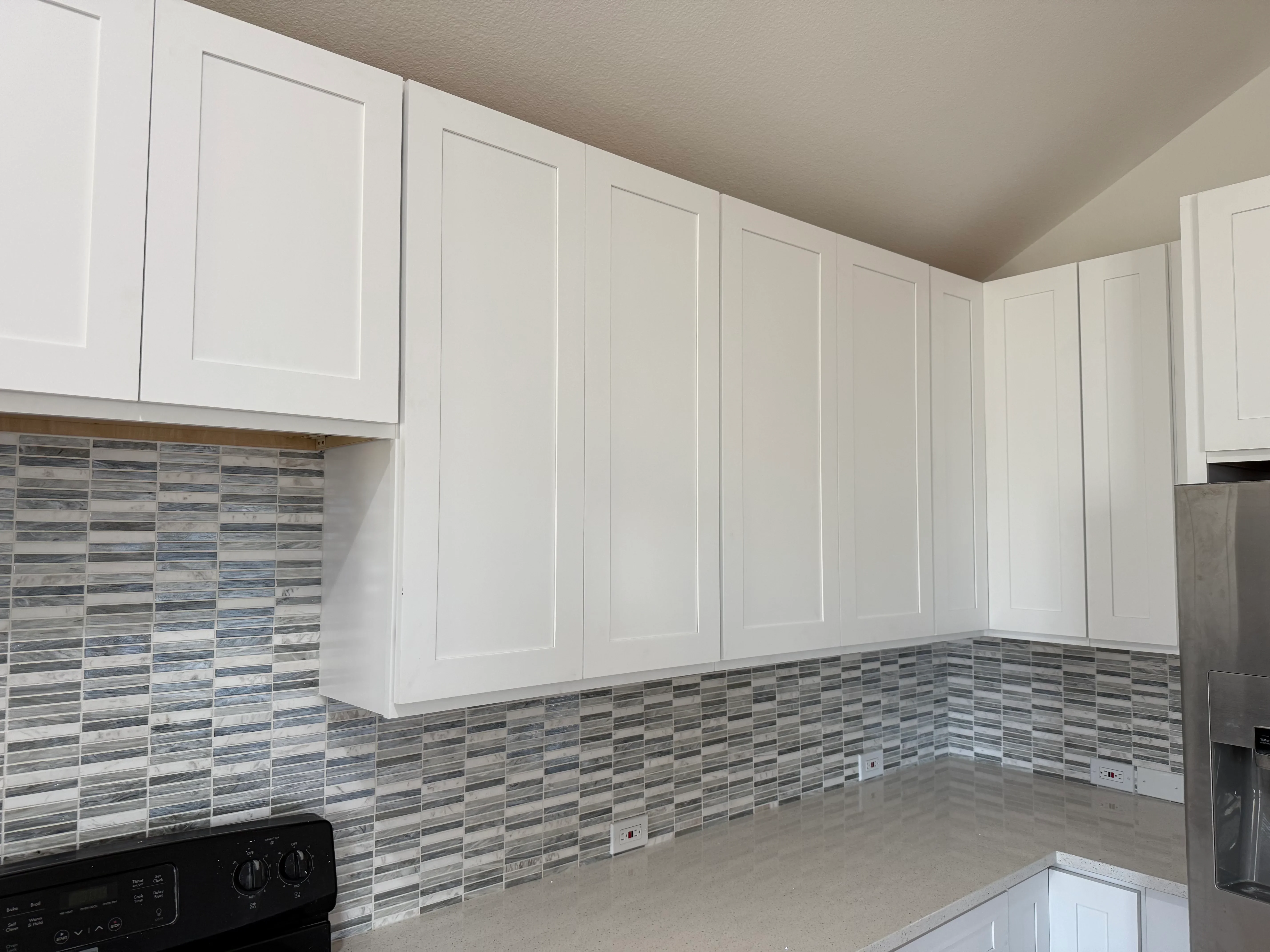 White kitchen cabinets with linear glass tile backsplash and quartz countertops