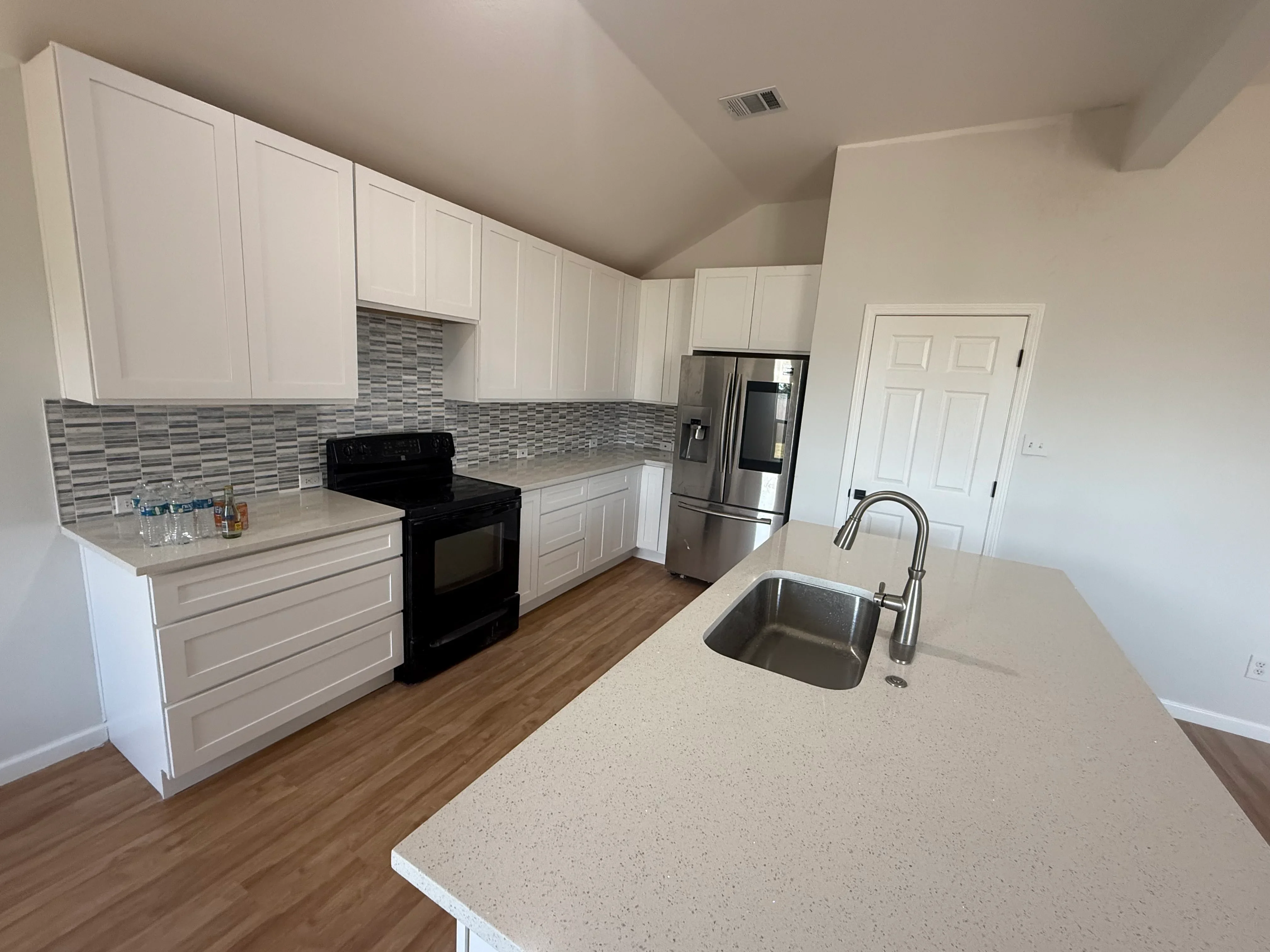 White kitchen cabinets, gray tile backsplash, quartz counters, stainless steel appliances, wood flooring