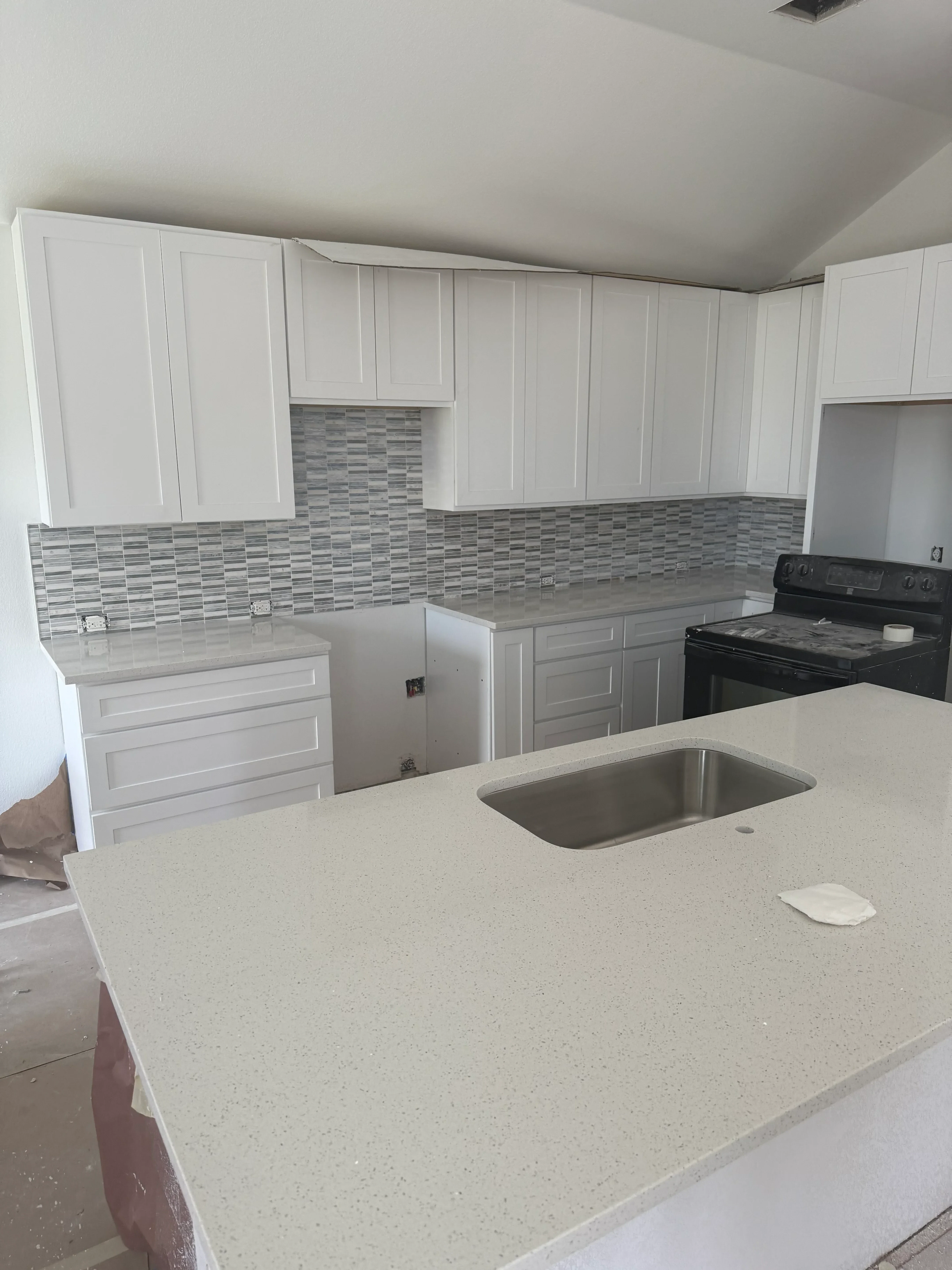 Kitchen with new gray patterned tile flooring, white cabinetry, and quartz countertops after water damage restoration
